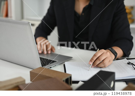 Architect working on laptop at a desk with material samples and house model in the foreground Architect working on laptop at a desk with material samples and house model in the foreground 119438978