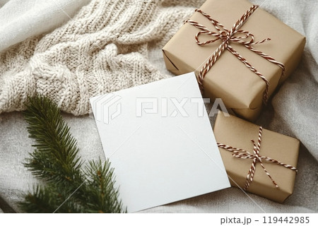Christmas greeting card mockup with gift box, knitted sweater and fir tree branch on linen background 119442985