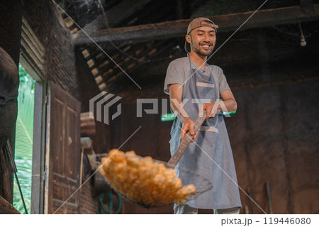 A skilled cook is expertly tossing up some golden fried food in a rustic kitchen setting A skilled cook is expertly tossing up some golden fried food in a rustic kitchen setting 119446080