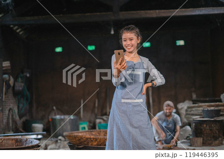 A Joyful Artisan Smiling While Actively Using Smartphone Inside His Workshop A Joyful Artisan Smiling While Actively Using Smartphone Inside His Workshop 119446395