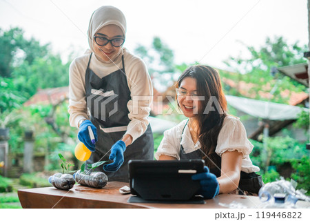 asian women looking at tablet while watering seedling 119446822