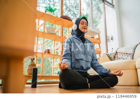A woman meditates peacefully at home, wearing headphones in a calming atmosphere 119446959