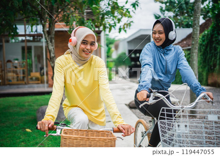 young veiled woman with friends cycling in front of the house 119447055