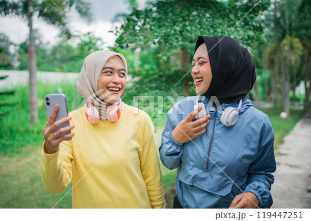 two beautiful hijab girls chatting and holding a smartphone while walking two beautiful hijab girls chatting and holding a smartphone while walking 119447251