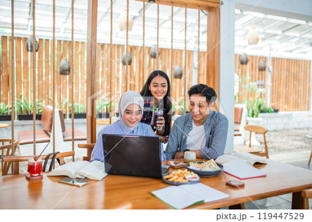 three university students use and look at a laptop together 119447529