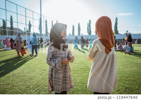 Two young girls converse happily outdoors on a sunny day, enjoying each others company 119447648
