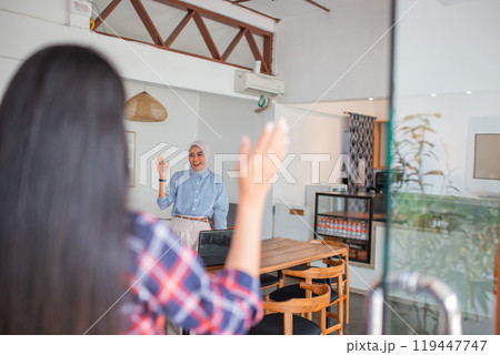 two Indonesian women meet with a waving gesture at a coffee shop 119447747