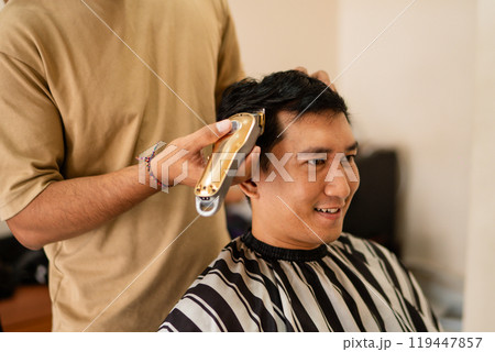 A man is currently getting his hair cut by a barber at a salon 119447857