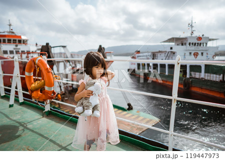 A child with a cherished doll enjoys a ferry ride among colorful boats in a harbor A child with a cherished doll enjoys a ferry ride among colorful boats in a harbor 119447973