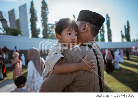 A Father Holding His Child in Traditional Attire at a Joyful Outdoor Gathering 119448016