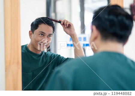A man is currently brushing his hair in front of a large mirror 119448082