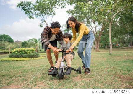 little boy riding a tricycle with mom and dad while playing in the park 119448279