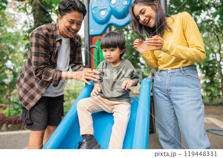 little boy playing slide with mom and dad in the park 119448331