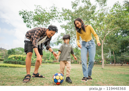 mom and dad told the son to kick the ball when playing together in the park mom and dad told the son to kick the ball when playing together in the park 119448368