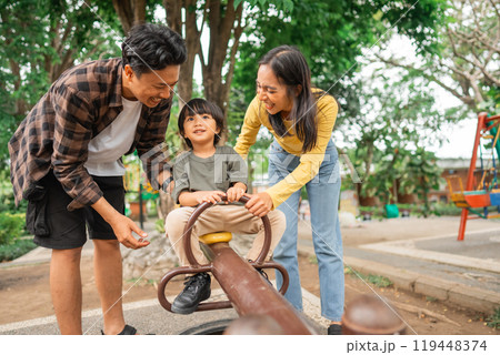 mom and dad accompany a little boy on a seesaw while playing together mom and dad accompany a little boy on a seesaw while playing together 119448374