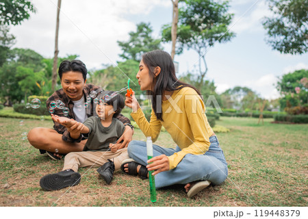 mom sits making bubbles as the boy and his dad catch mom sits making bubbles as the boy and his dad catch 119448379