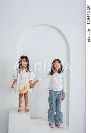 Two little girls joyfully stand together, holding hands tightly 119448420