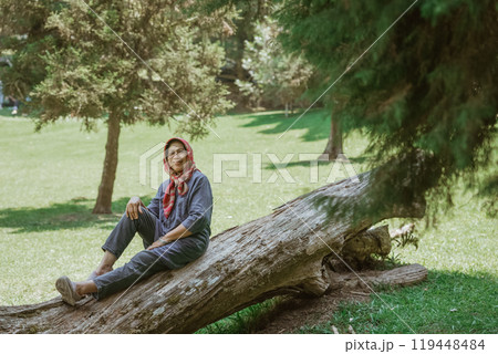 A woman, with great grace, is posing elegantly on a fallen tree located in a scenic park A woman, with great grace, is posing elegantly on a fallen tree located in a scenic park 119448484