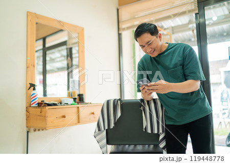 A man is currently standing inside a barber shop while looking at his phone 119448778