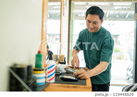 A man is currently standing at a barber shop while cutting a customer s hair A man is currently standing at a barber shop while cutting a customer s hair 119448820