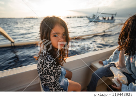 A little girl is happily sitting on a small boat in the vast ocean 119448925