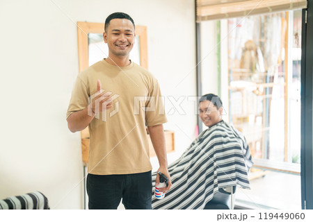 A man gives a thumbs up while getting a haircut at a barber 119449060