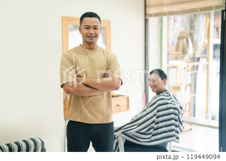 A man stands next to another getting his hair cut in a barber shop 119449094