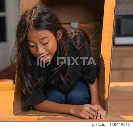 A young child happily playing inside a cardboard box in a cozy indoor setting 119449178