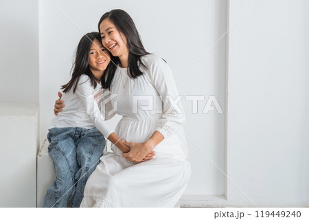 A pregnant woman is comfortably seated next to a little girl on a couch 119449240