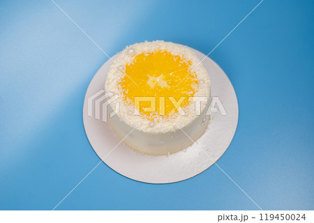 Small coconut cake decorated with an orange slice and white pearls on blue background Small coconut cake decorated with an orange slice and white pearls on blue background 119450024