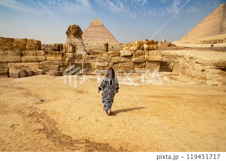 A rear view of a woman in a long traditional Muslim dress looking at the 3 great Pyramids in Egypt A rear view of a woman in a long traditional Muslim dress looking at the 3 great Pyramids in Egypt 119451717