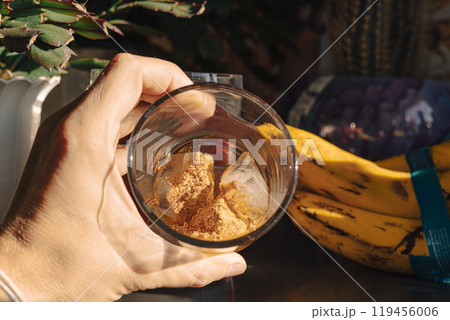 A glass filled with ice cubes and powdered Amanita muscaria mushroom on its surface, held in the hand, illuminated by natural sunlight. Preparing a homemade fly agaric elixir A glass filled with ice cubes and powdered Amanita muscaria mushroom on its surface, held in the hand, illuminated by natural sunlight. Preparing a homemade fly agaric elixir 119456006