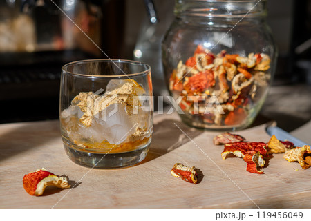 Preparation of fly agaric drink, ground powdered dry mushroom on ice cubes in a glass, illuminated by natural sunlight.  Homemade fly agaric elixir.   119456049