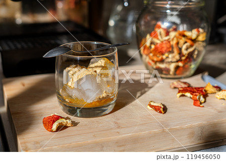 Preparation of fly agaric drink, ground powdered dry mushroom on ice cubes in a glass, illuminated by natural sunlight.  Homemade fly agaric elixir.   119456050