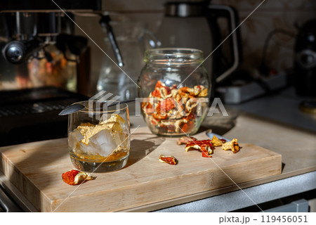 Preparation of fly agaric drink, ground powdered dry mushroom on ice cubes in a glass, illuminated by natural sunlight.  Homemade fly agaric elixir.   119456051