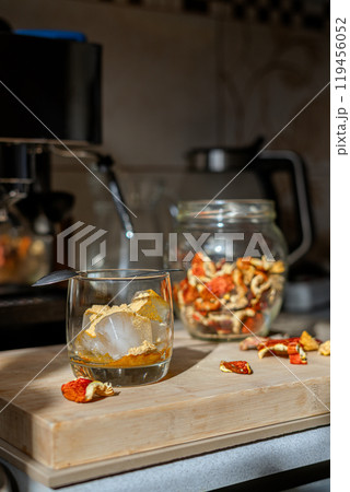 Preparation of fly agaric drink, ground powdered dry mushroom on ice cubes in a glass, illuminated by natural sunlight.  Homemade fly agaric elixir.   119456052