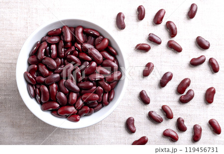 Dried kidney beans in a white bowl on linen fabric. Raw, uncooked, red common kidney beans, a variety of the bean Phaseolus vulgaris, a vegetarian staple food, and commonly used in chili con carne. 119456731