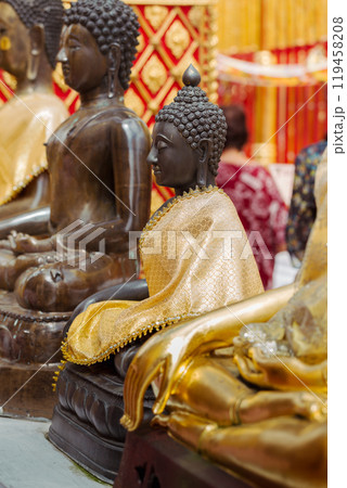 Buddhist statues adorned with golden robes in a temple. 119458208