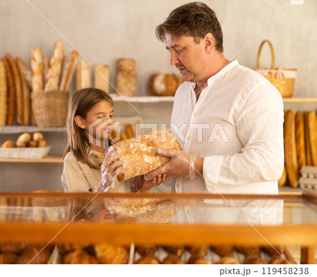 Dad and daughter customers holding loaf of bread and baguettes with hands in disposable gloves Dad and daughter customers holding loaf of bread and baguettes with hands in disposable gloves 119458238