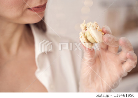Woman holding macaron in gloved hand, emphasizing hygiene and culinary delight Woman holding macaron in gloved hand, emphasizing hygiene and culinary delight 119461950