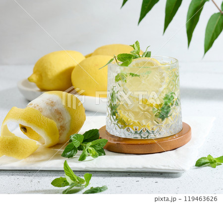Transparent glass with lemon slices, mint leaves and ice cubes on white table Transparent glass with lemon slices, mint leaves and ice cubes on white table 119463626