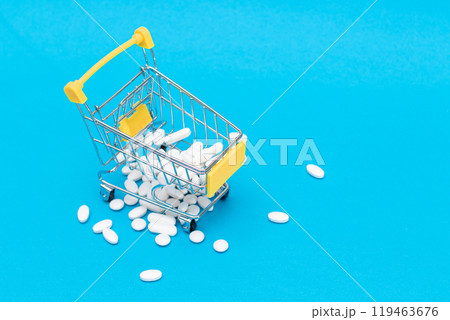 Scattered Pills or Capsules and Shopping Cart on Blue Background Scattered Pills or Capsules and Shopping Cart on Blue Background 119463676