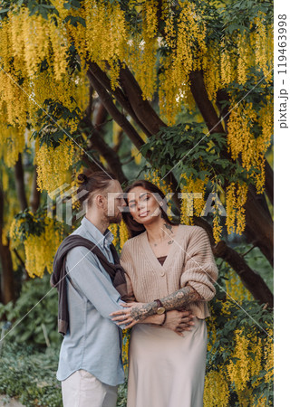 Amazing couple hugging under tree with yellow tree. Lovers couple hugging in a laburnum tree. Couple lovers hugging in the park. Girl with tattoos. A girl and a boy kiss. Amazing couple hugging under tree with yellow tree. Lovers couple hugging in a laburnum tree. Couple lovers hugging in the park. Girl with tattoos. A girl and a boy kiss. 119463998