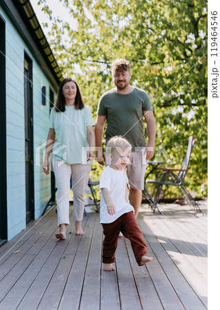 A joyful family walking together on a sunny day, with their child leading the way in playful moment A joyful family walking together on a sunny day, with their child leading the way in playful moment 119464546