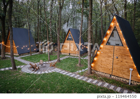 Modern wooden A-frame cabins in forest with outdoor seating and fire pit area, relaxation time 119464550