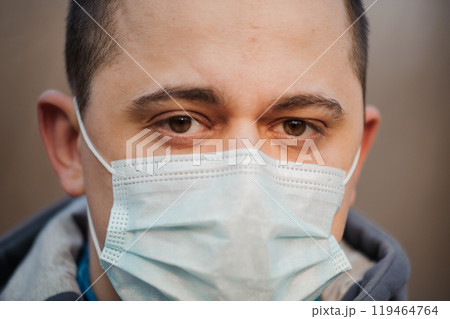Intense Gaze of a Man Wearing a Surgical Mask in Urban Environment Intense Gaze of a Man Wearing a Surgical Mask in Urban Environment 119464764
