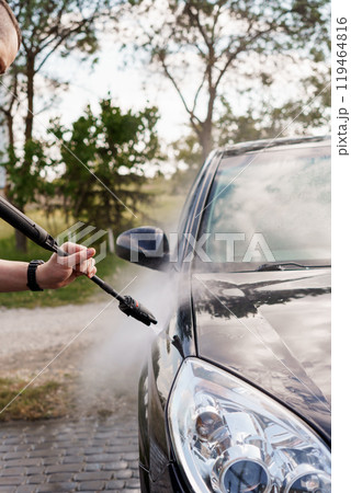 Detailed Close-Up of a Person Using a Pressure Washer to Clean a Black Car in a Scenic Outdoor Setting 119464816