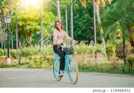 Portrait of smiling young woman riding a bicycle in a nice park. Happy girl riding a bicycle in a park at sunset 119466932