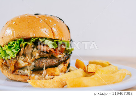 Big cheeseburger with fries served with copy space. Homemade burger with french fries on a plate on wooden table Big cheeseburger with fries served with copy space. Homemade burger with french fries on a plate on wooden table 119467398