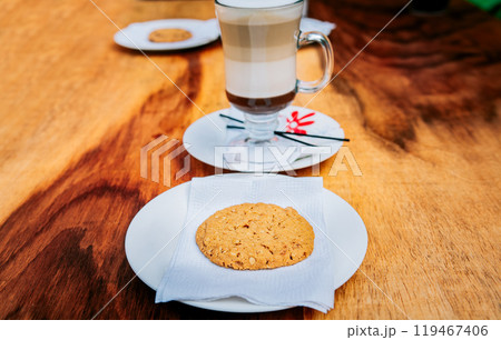 Close up of biscuit with cappuccino on wooden table. Delicious glass of hot cappuccino with cookie on wooden background 119467406